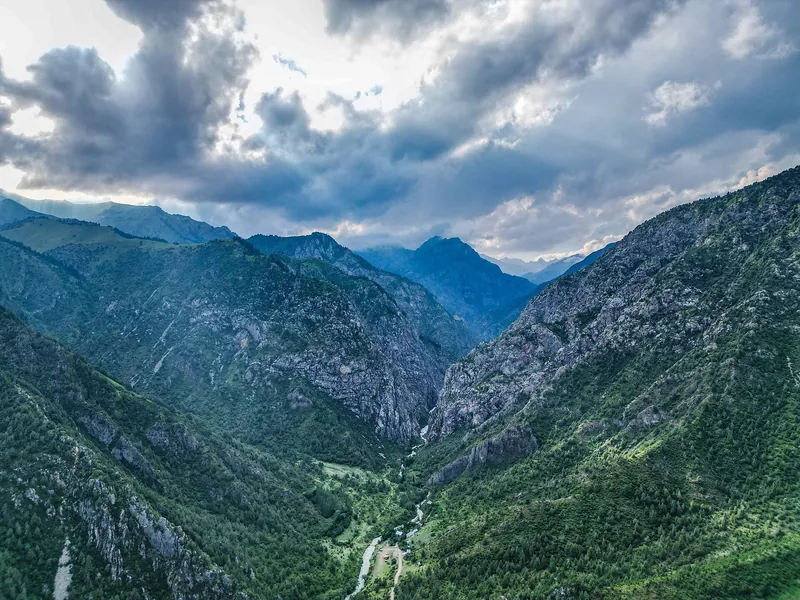 Un denso bosque cubre las laderas de un valle montañoso y pesadas nubes se acumulan sobre las crestas.