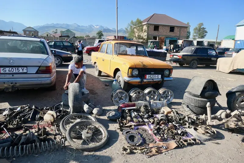 Los repuestos y las ruedas están colocados en el suelo, detrás de ellos hay autos y montañas.