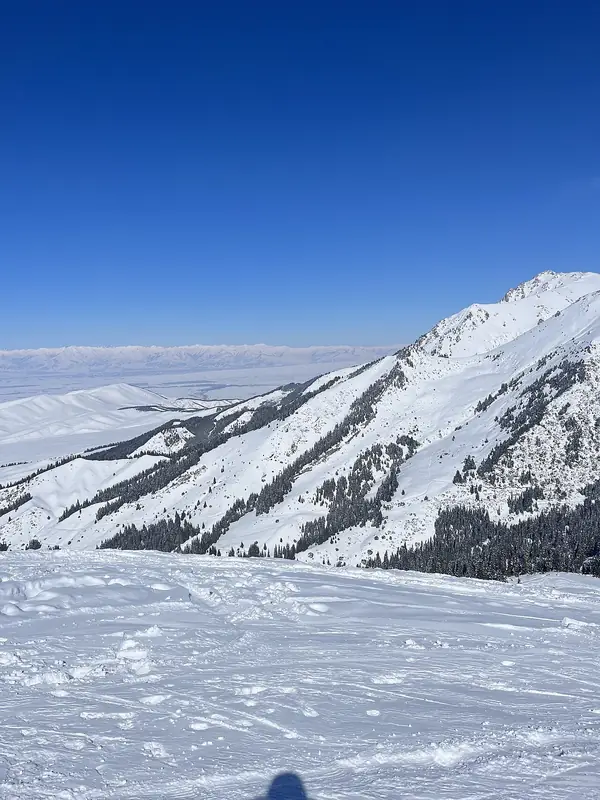 Ladera y cresta nevadas, nubes y llanura abajo