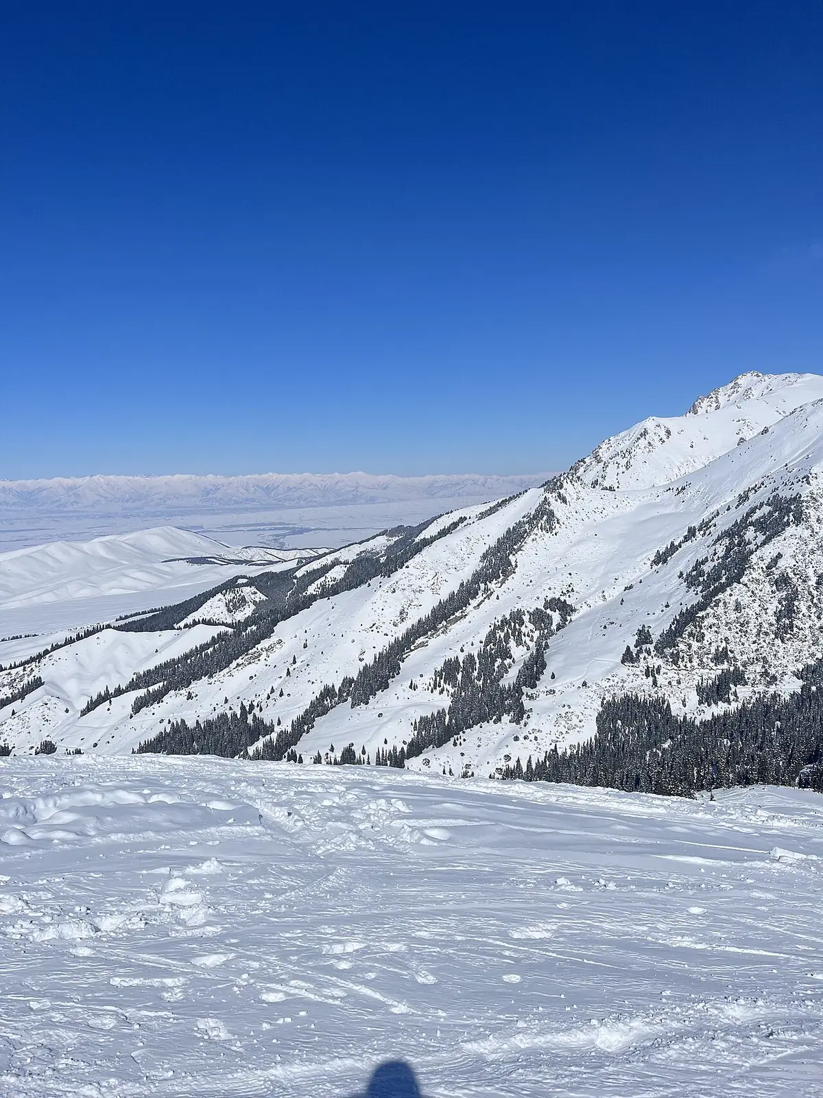 Ladera y cresta nevadas, nubes y llanura abajo