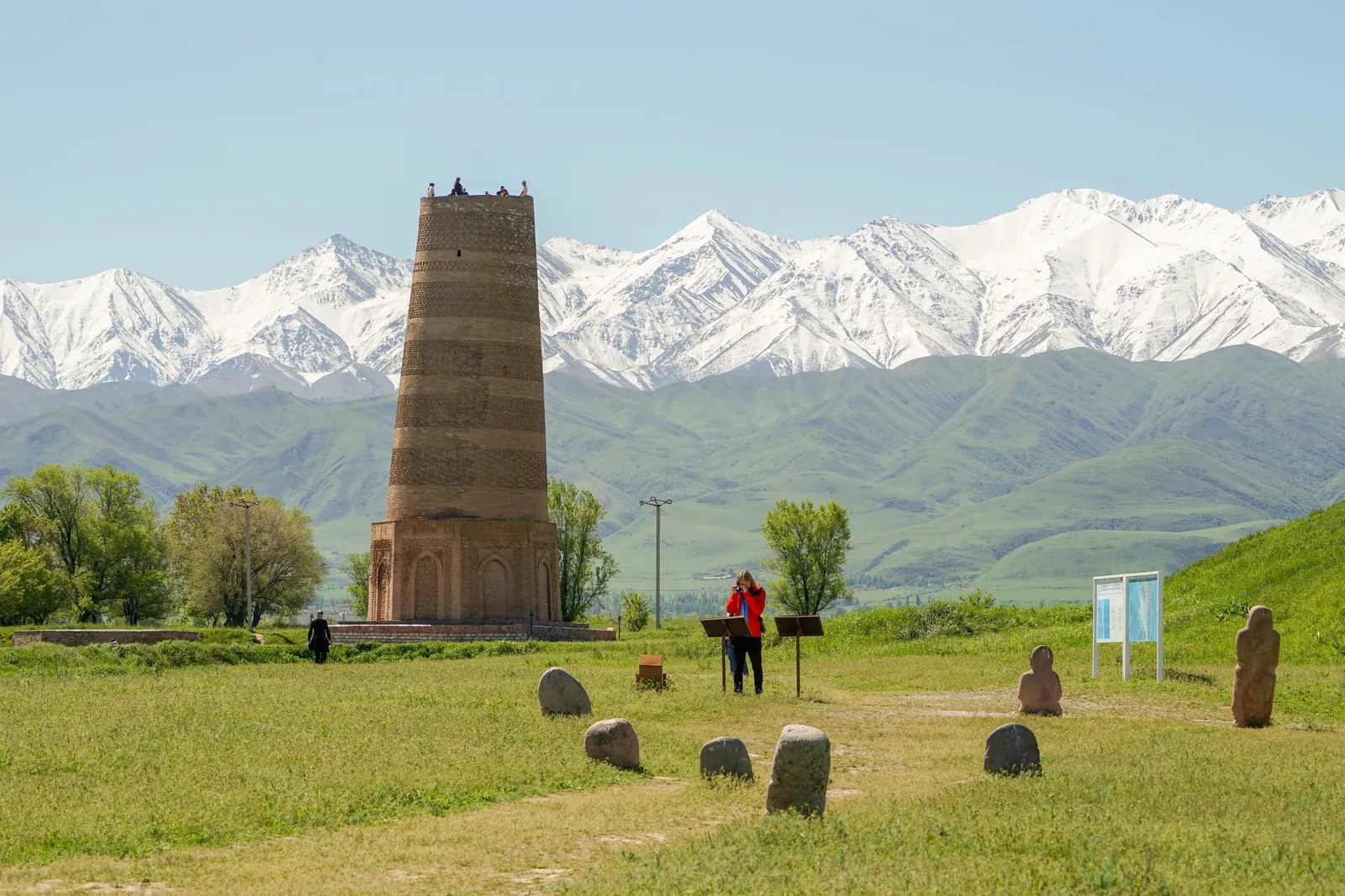 Brick tower and stone sculptures on a green lawn in front of a snowy mountain range.
