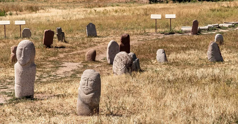 Several stone figures stand together on a grassy area of the ancient town site.
