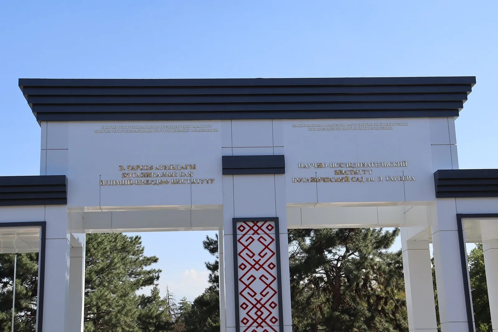 The botanical garden’s white gates with a dark cornice and ornament, with trees visible behind.