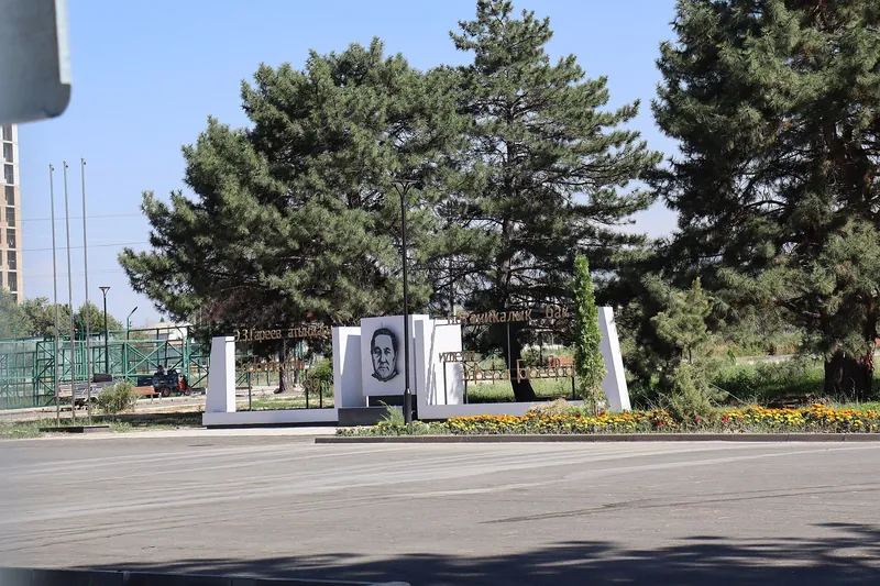 植物园围栏旁的纪念展板上有肖像，后方生长着高大的针叶树。