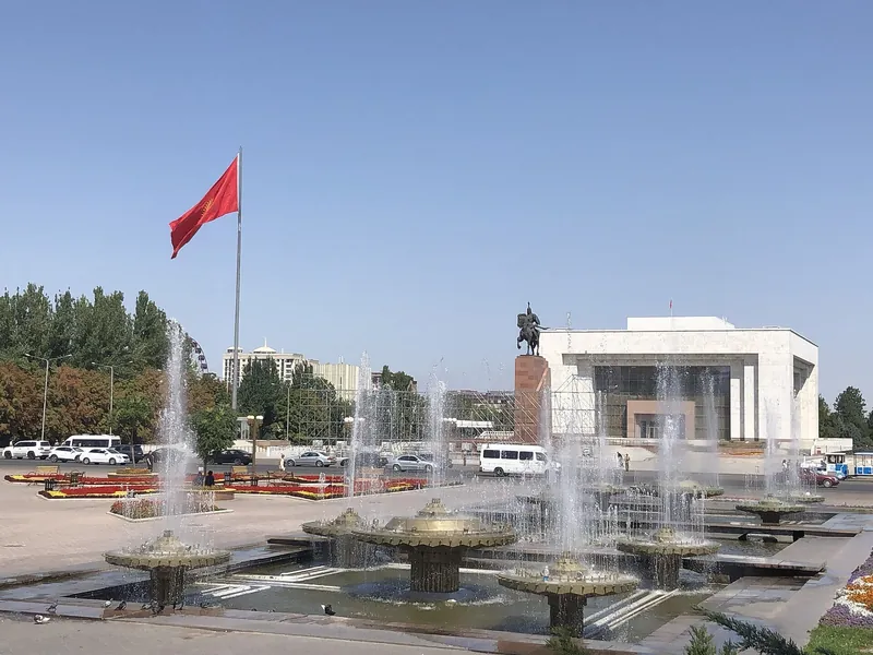 Rote Flagge über dem Ala-Too-Platz; vor den Gebäuden liegen Blumenbeete und Brunnenbecken.