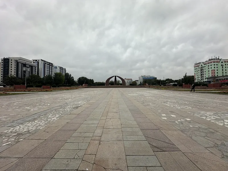 낮게 깔린 회색 구름 아래 넓은 포장 광장이 아치형 기념 시설로 이어진다.