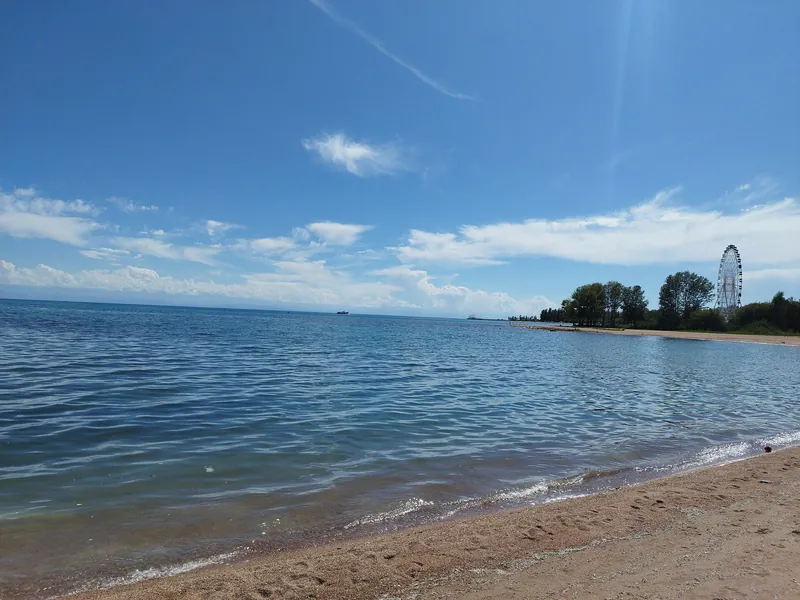 Das Wasser des Sees nähert sich dem Sandstrand und in der Ferne ist am Ufer ein Riesenrad zu sehen.