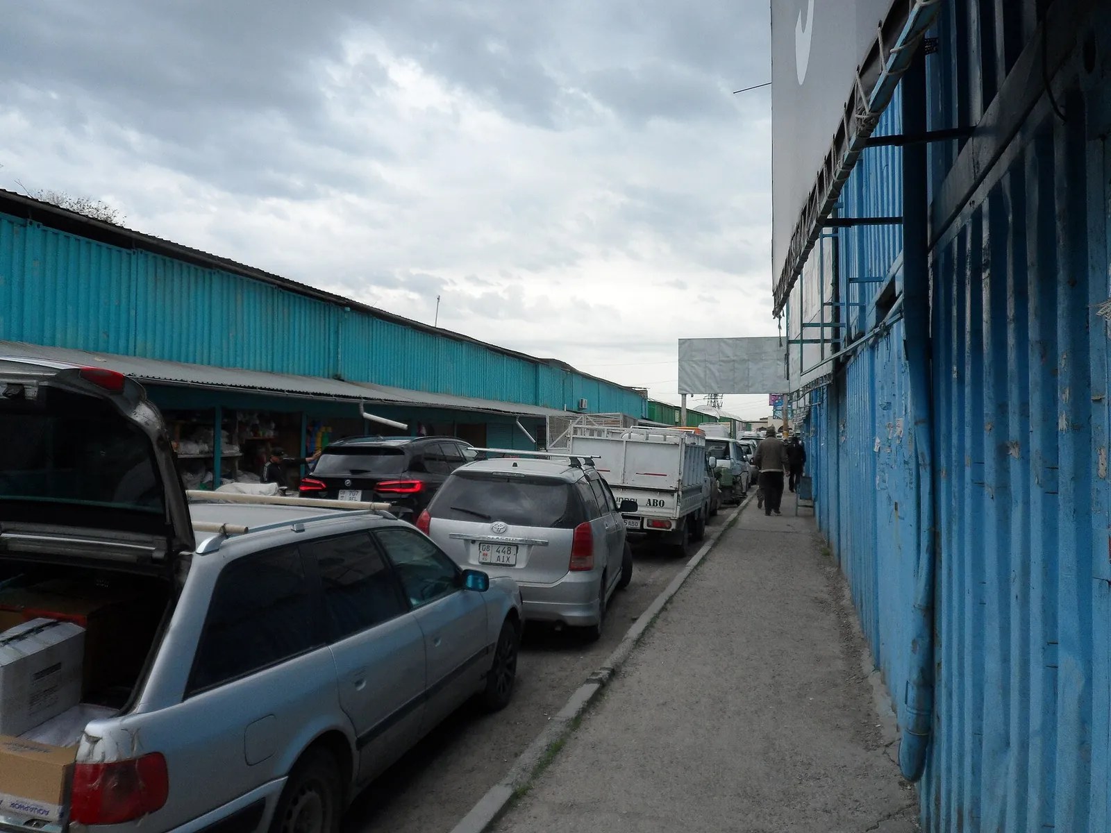 Eine schmale Gasse mit geparkten Autos zwischen Reihen mit blauen Metallwänden.