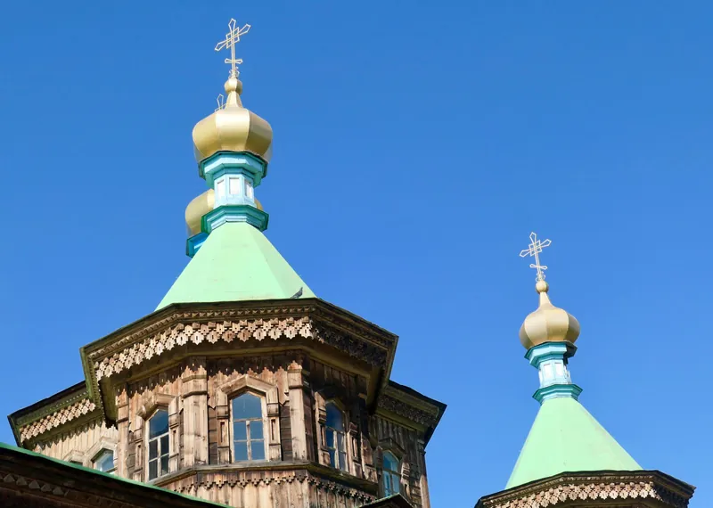 Goldene Kuppeln mit Kreuzen über hölzernen Türmen unter blauem Himmel.