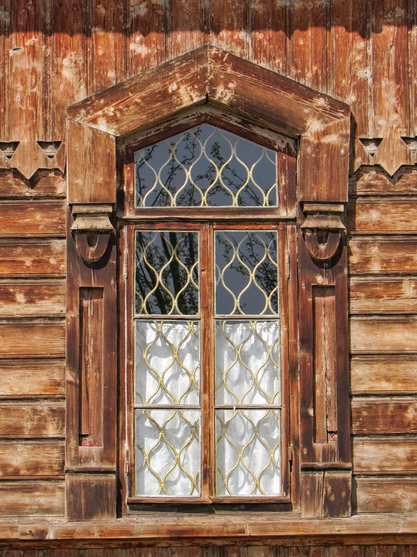 Hohes Holzfenster mit dekorativen Schnitzereien und Glas mit Metallrahmen.