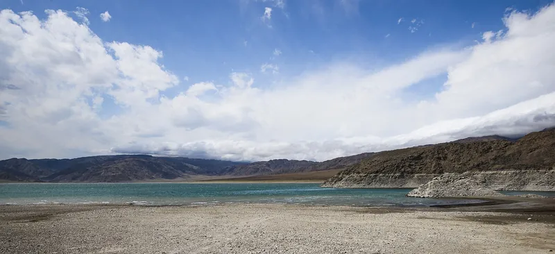 Une rive claire et pierreuse rejoint une baie étroite sous de grands nuages blancs.