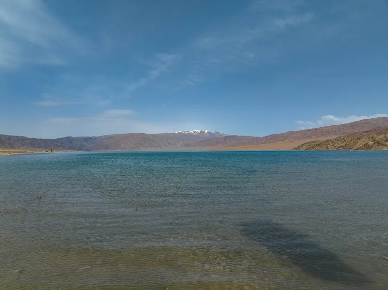 L’eau limpide près de la rive douce du réservoir, avec des montagnes brunes et sèches au-delà.