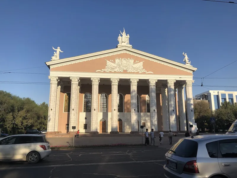 Säulenportikus und Dreiecksgiebel des Opern- und Balletttheaters, davor eine Straße mit Passanten.