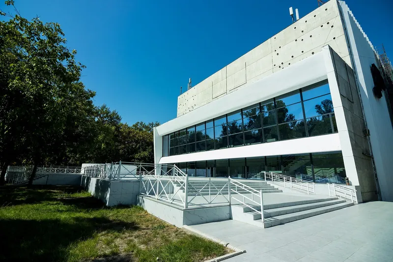 Helle Fassade des russischen Schauspieltheaters mit Glasgalerie und Rampe vor dem Eingang.