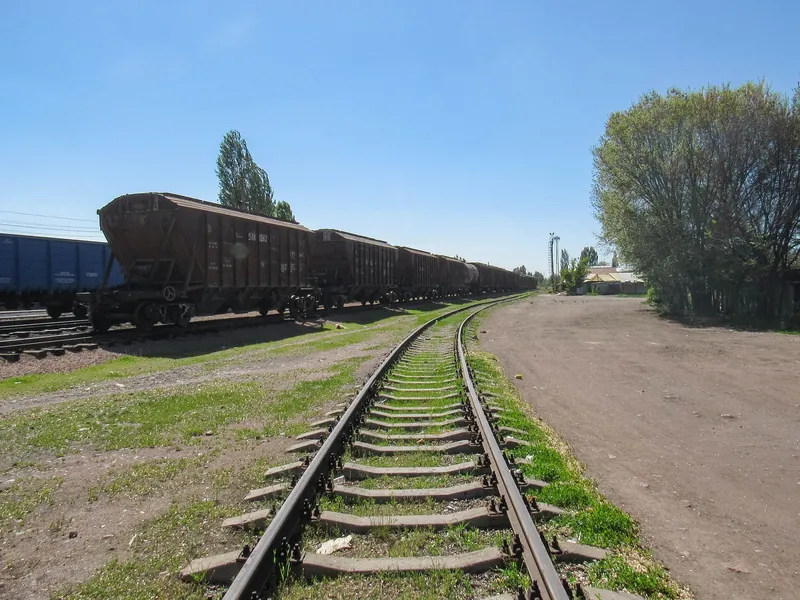 Güterwagen auf den Gleisen des Bahnhofs Kant, in der Nähe gibt es eine Kurve in den Schienen und Bäume in der Nähe der unbefestigten Straße.
