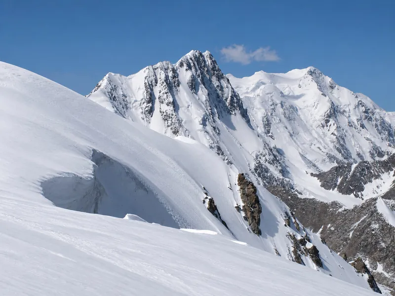 Verschneiter Berggipfel über einem Gletscher und dunkle Felshänge im Frühlingslicht.