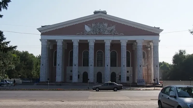 Säulenfassade des Opern- und Balletttheaters mit dreieckigem Giebel, davor eine Stadtstraße.