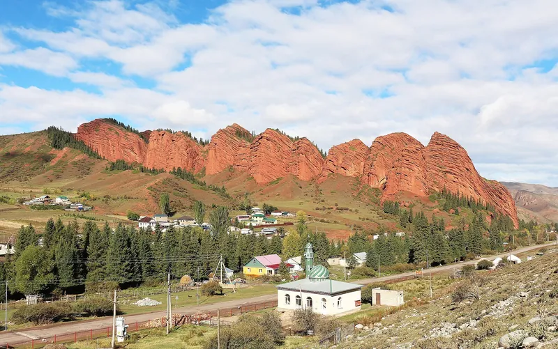Fila de torres de roca roja sobre árboles y pequeñas casas del valle.