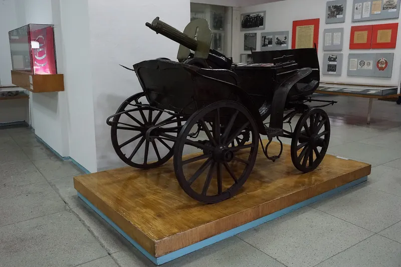 Gerobak dengan senapan mesin di podium kayu di aula museum, di belakangnya terdapat stand dengan dokumen.