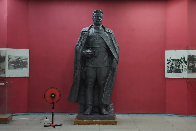 Patung perunggu Frunze di depan dinding merah aula museum dengan bahan bersejarah.