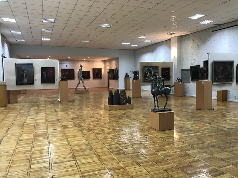 Просторный музейный зал с картинами и скульптурами, пол выложен деревянным паркетом.