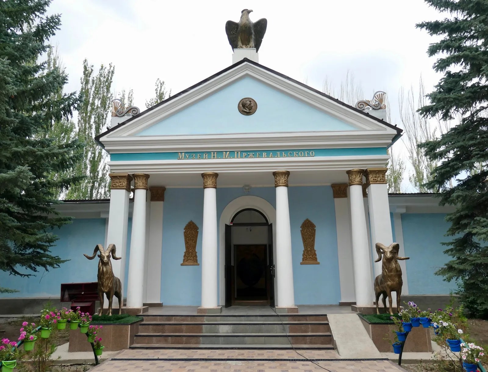 Museo bianco con colonne azzurre e portico, con un ornamento scultoreo sopra l’ingresso.