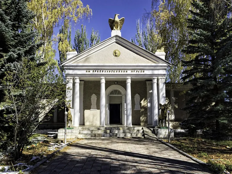 Il museo con colonne blu e portico bianco è visibile tra gli alberi verdi.