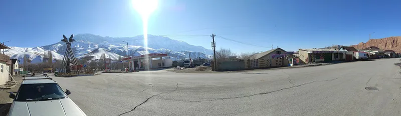 Une large rue à l’entrée de la ville, entourée de maisons basses, avec des montagnes enneigées au loin.