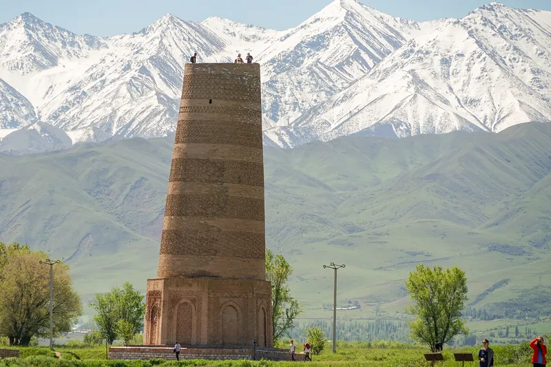 Backsteinturm auf offener grüner Ebene vor einer fernen verschneiten Bergkette.