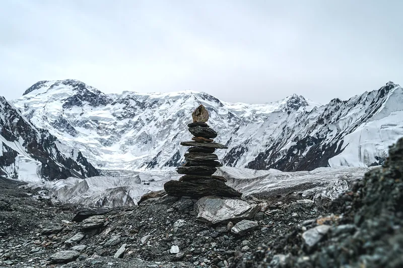 A stone cairn on the rocky surface of South Engilchek Glacier, with Jengish Chokusu in the distance