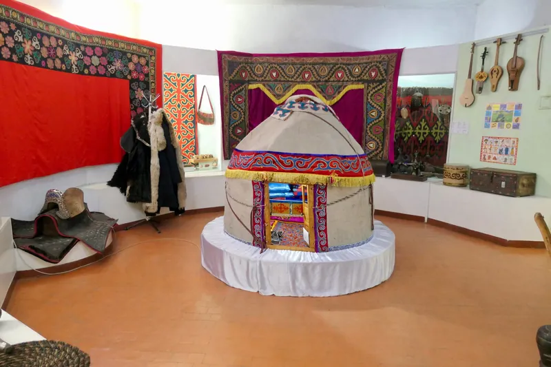 Maqueta de yurta y objetos cotidianos en una sala del museo, con tejidos y alfombras en las paredes.