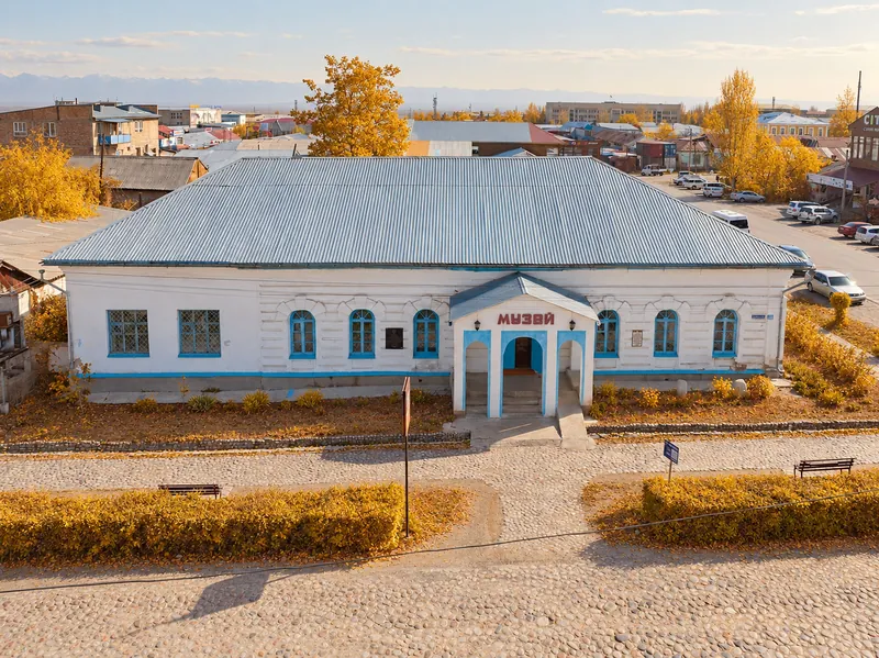 Museo Histórico Karakol en otoño, con follaje amarillo alrededor del edificio blanco.