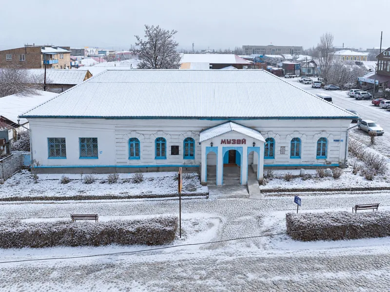 Museo Histórico Karakol en invierno: edificio blanco y patio bajo una fina nieve.
