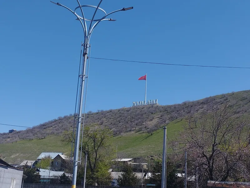 Bandera roja en lo alto de la pendiente, con una farola y árboles en primer plano.