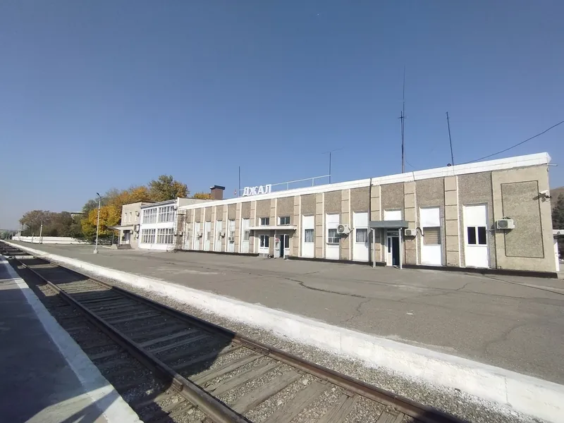 Una luminosa estación de tren junto a un andén vacío, las vías se alejan a lo lejos a la izquierda.