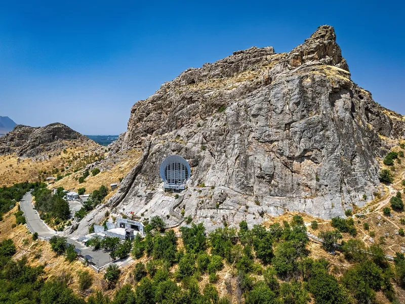 La entrada redondeada del museo está integrada en la roca; escaleras suben hacia ella entre piedras y árboles dispersos.