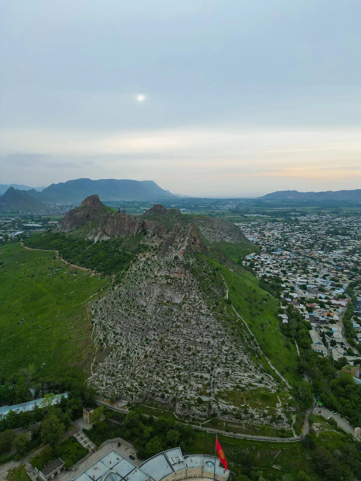 Una cresta rocosa estrecha se alza sobre la ciudad; las laderas verdes bajan hacia una zona densamente edificada.