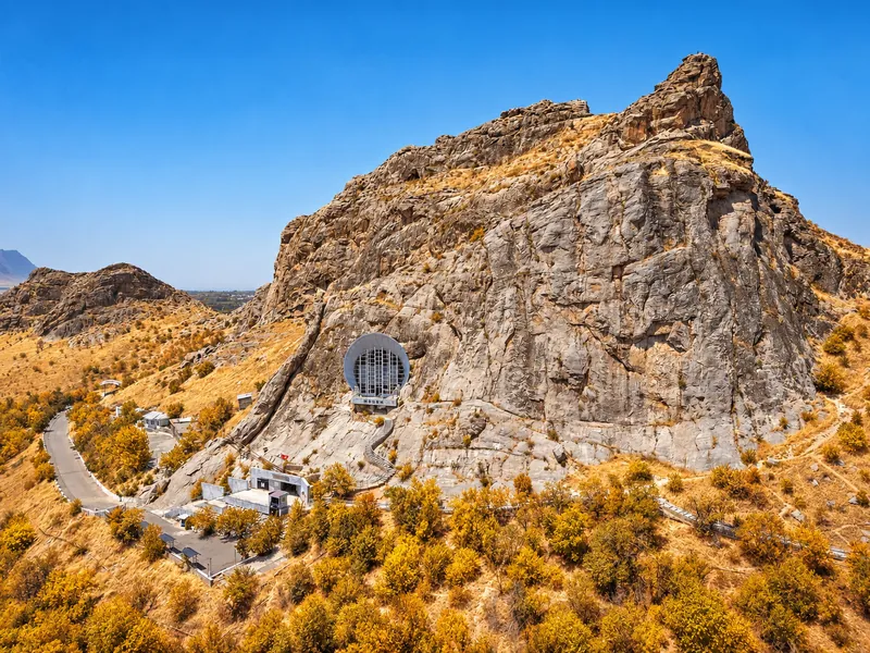 Vista otoñal del acantilado Montaña sagrada de Sulaiman-Too con la entrada a la cueva y vegetación dorada.