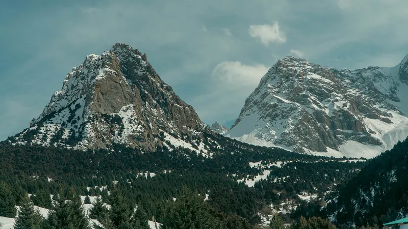 Cime innevate e torri di pietra si ergono sopra un'oscura foresta di conifere in una valle di montagna.